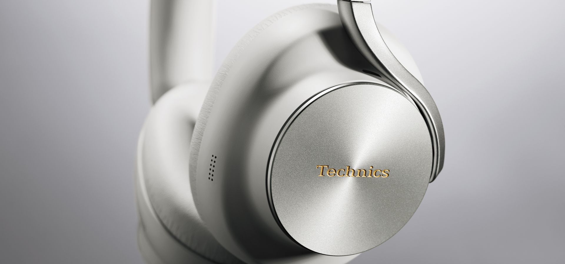Technics EAH-A1000E-S Technics EAH-A1000 bezprzewodowe słuchawki z adaptacyjną redukcją szumów ANC (parowanie wielopunktowe Bluetooth, LDAC, do 45H pracy z ANC), srebrne 16 Zbliżenie na obudowę Technics EAH-A1000 w kolorze szaro-beżowym i złote logo Technics.