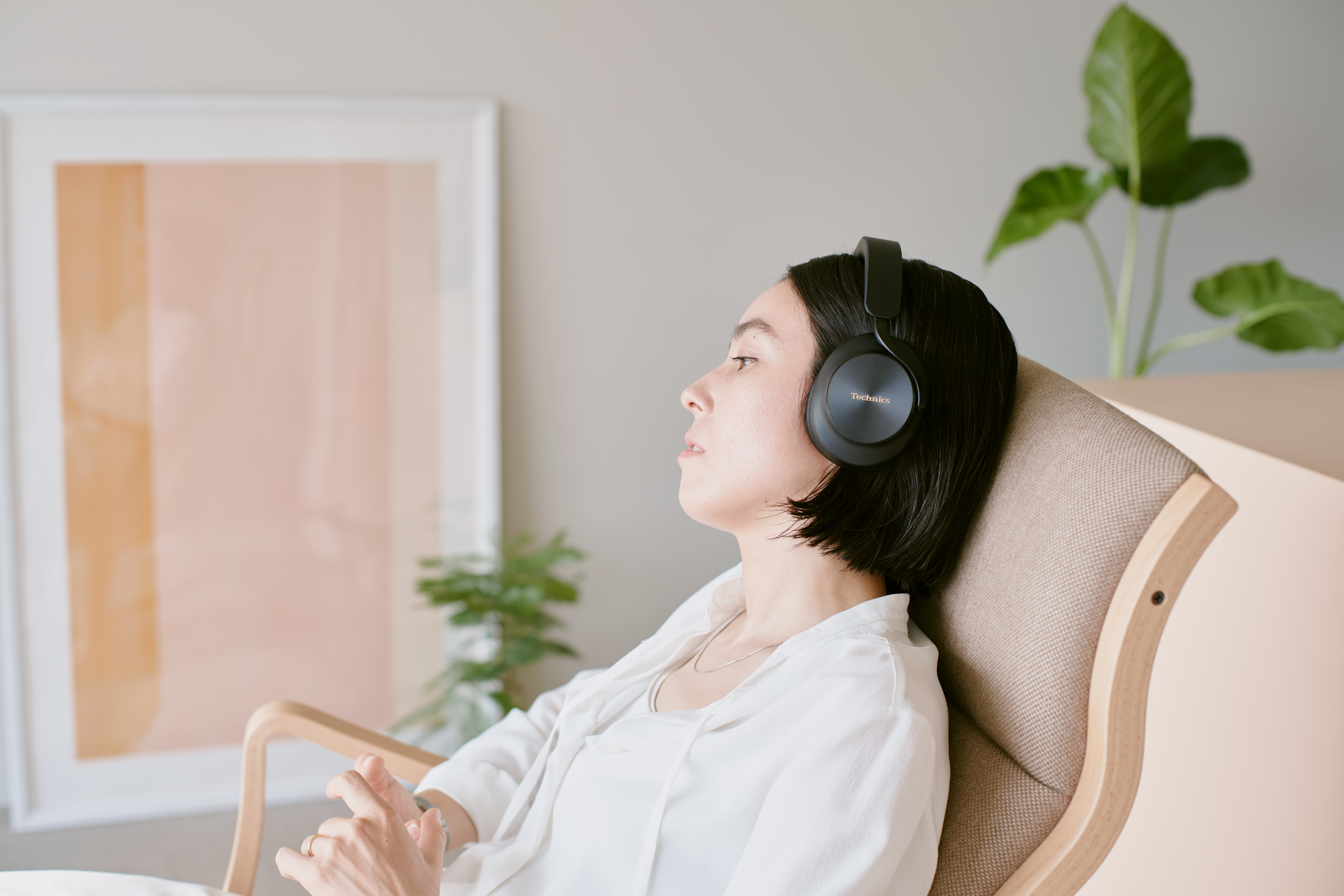 Technics EAH-A1000E-S Technics EAH-A1000 bezprzewodowe słuchawki z adaptacyjną redukcją szumów ANC (parowanie wielopunktowe Bluetooth, LDAC, do 45H pracy z ANC), srebrne 41 Kobieta odpoczywająca w domu w czarnych słuchawkach nausznych marki Technics.