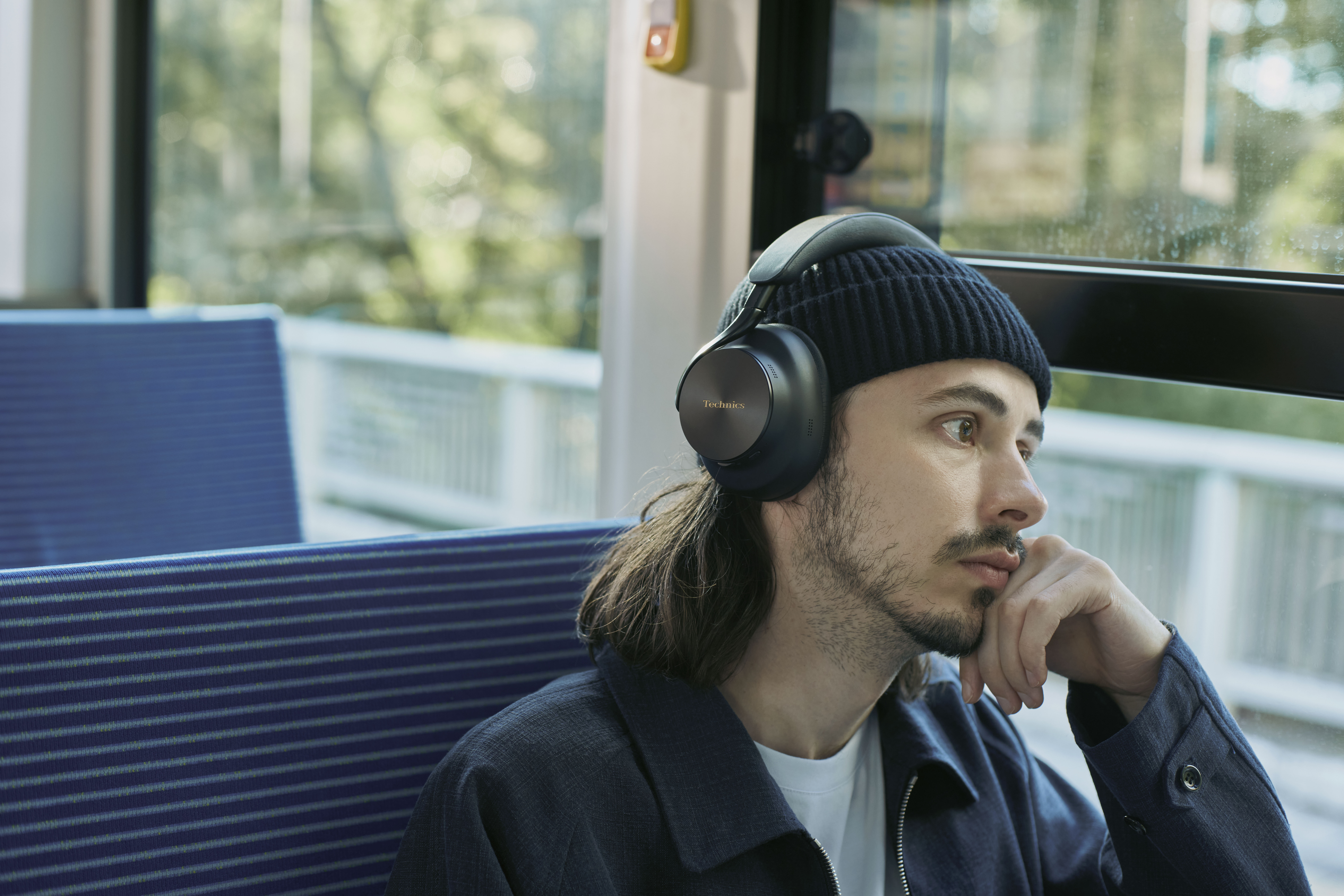 Technics EAH-A1000E-S Technics EAH-A1000 bezprzewodowe słuchawki z adaptacyjną redukcją szumów ANC (parowanie wielopunktowe Bluetooth, LDAC, do 45H pracy z ANC), srebrne 47 Mężczyzna w słuchawkach nausznych marki Technics podczas podróży pociągiem.